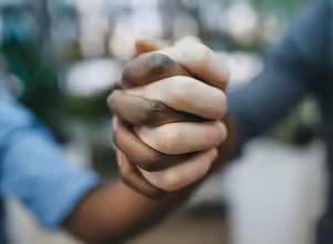 white and black skinned individuals holding hands supporting each other